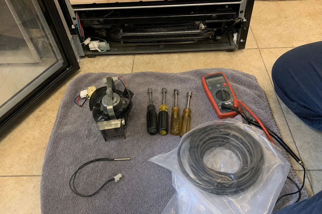 The same lay-out mirrored: meter, drivers, replacement fan motor, coiled gasket and sensor set out beside an opened appliance