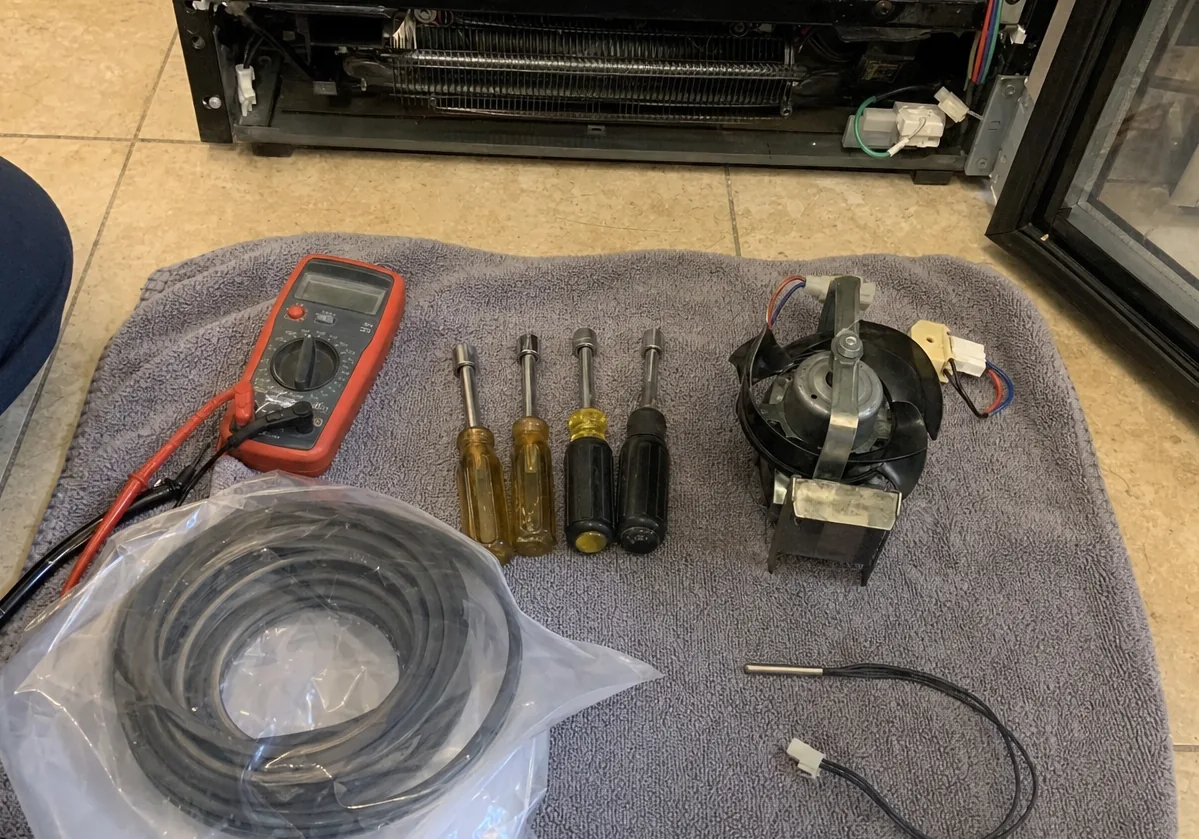 A bagged replacement door gasket and a temperature sensor waiting on the towel beside an opened cabinet