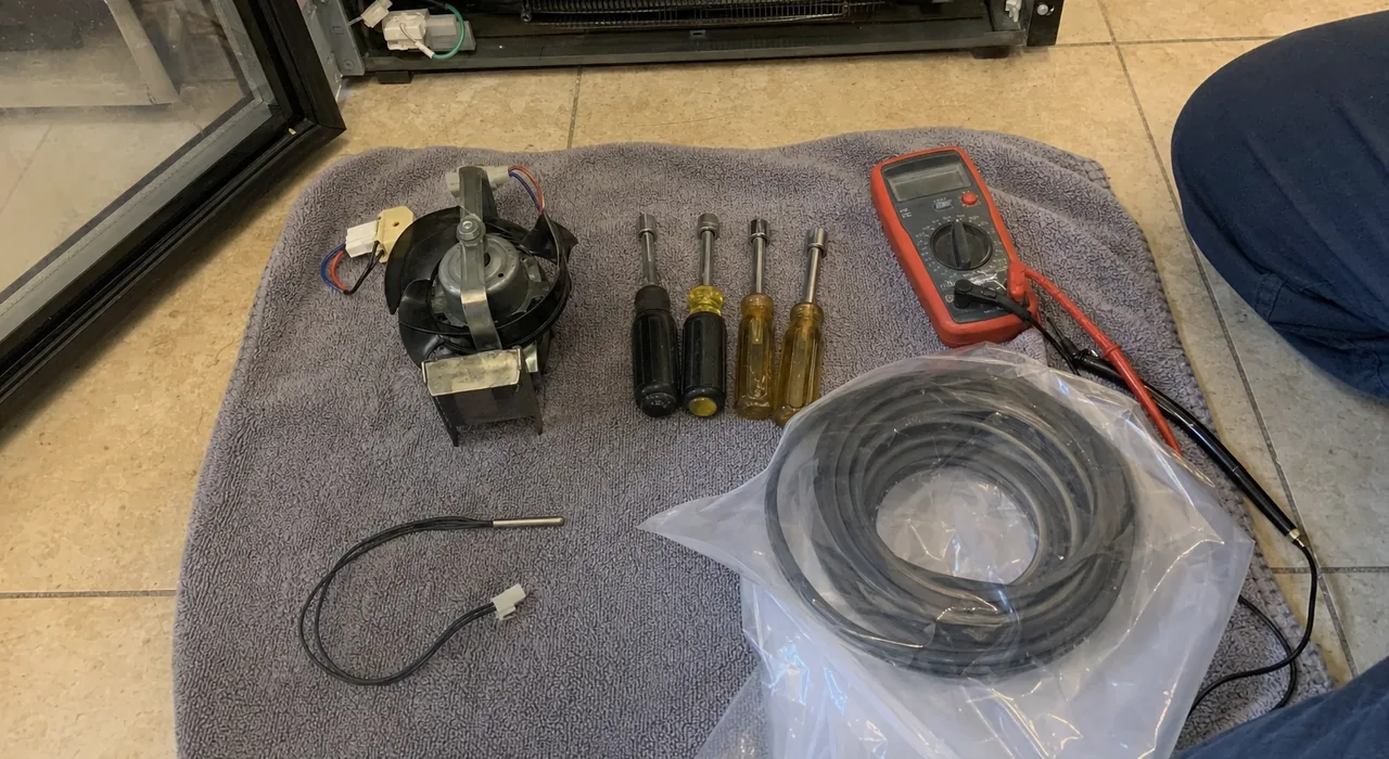 Floor-level view of a job in progress: tools and replacement parts on a grey towel in front of an open appliance